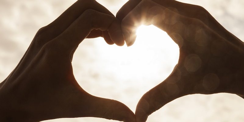 Hand heart shape silhouette made against the sun & sky of a sunr